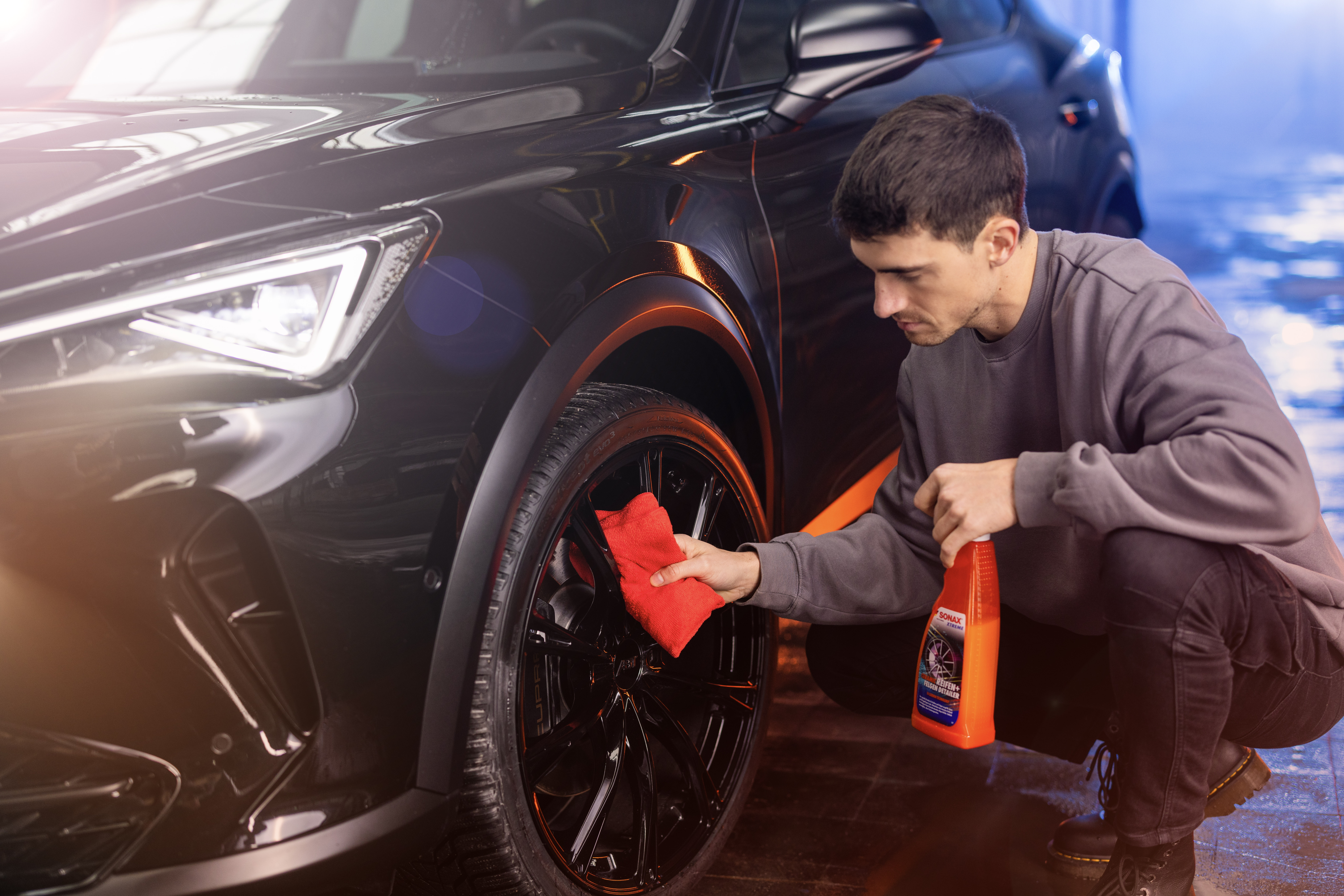 Man cleans rim with red microfiber cloth and tire+rim detailer from SONAX