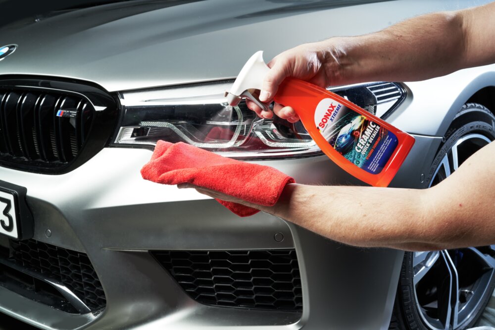 Jemand sprüht Detailer auf ein rotes Mikrofasertuch, um das Auto damit zu behandeln.