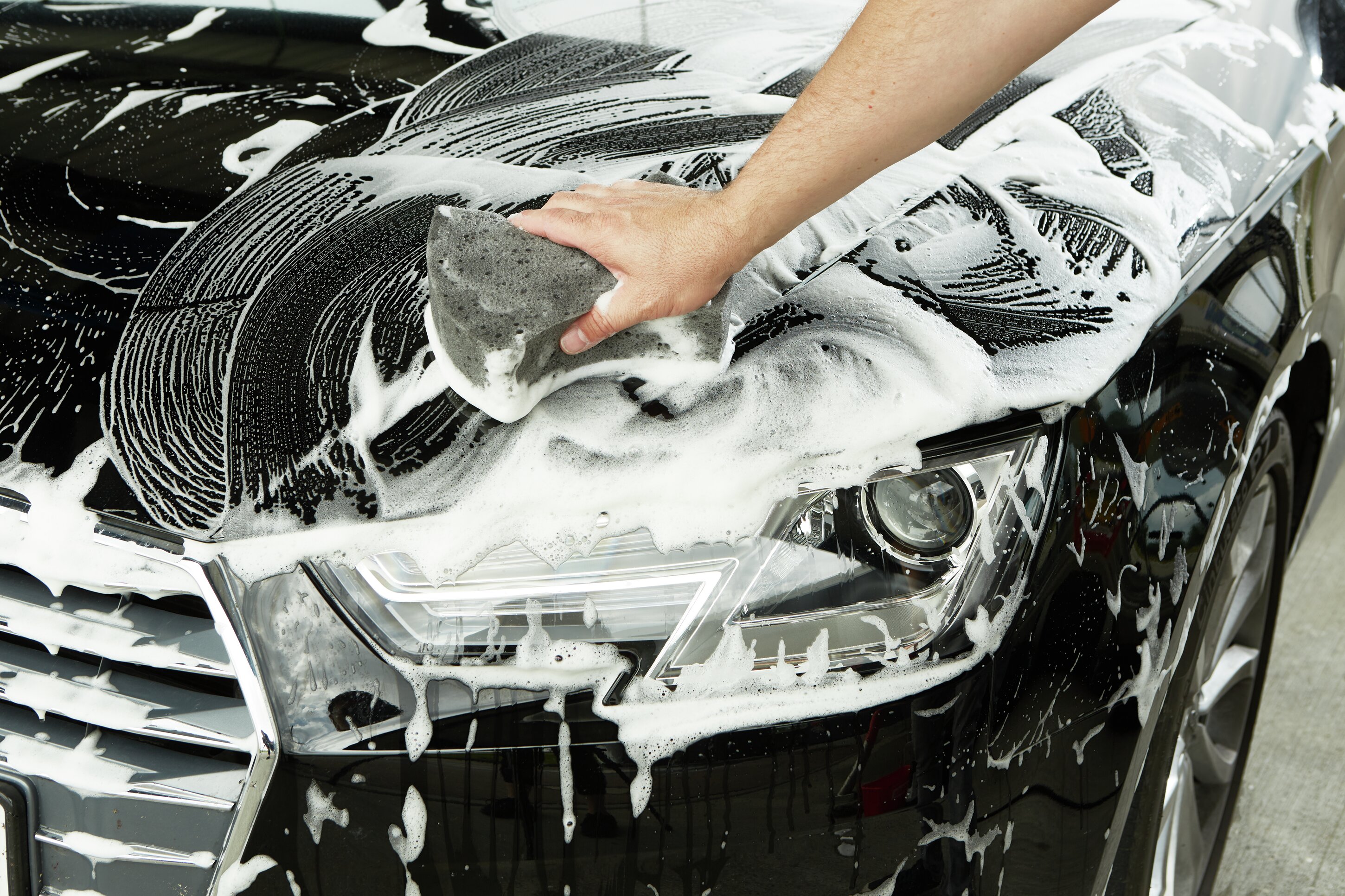 Mit einem Schwamm wird eine Motorhaube einshamponiert