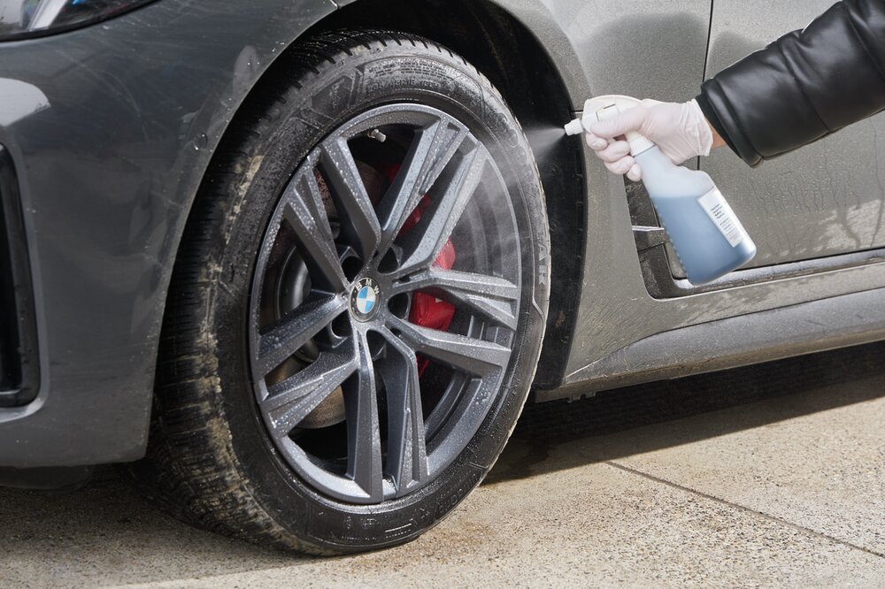 Felgenreiniger wird auf die Felge eines weißen Autos gesprüht