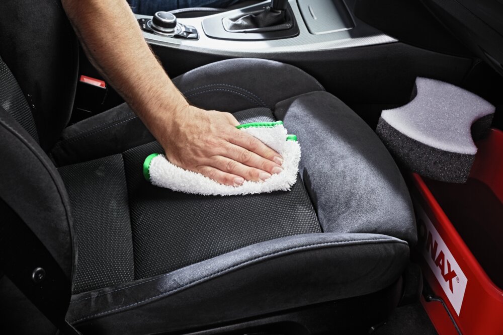 Ein Autositz wird mit einem weißen Mikrofasertuch gereinigt.