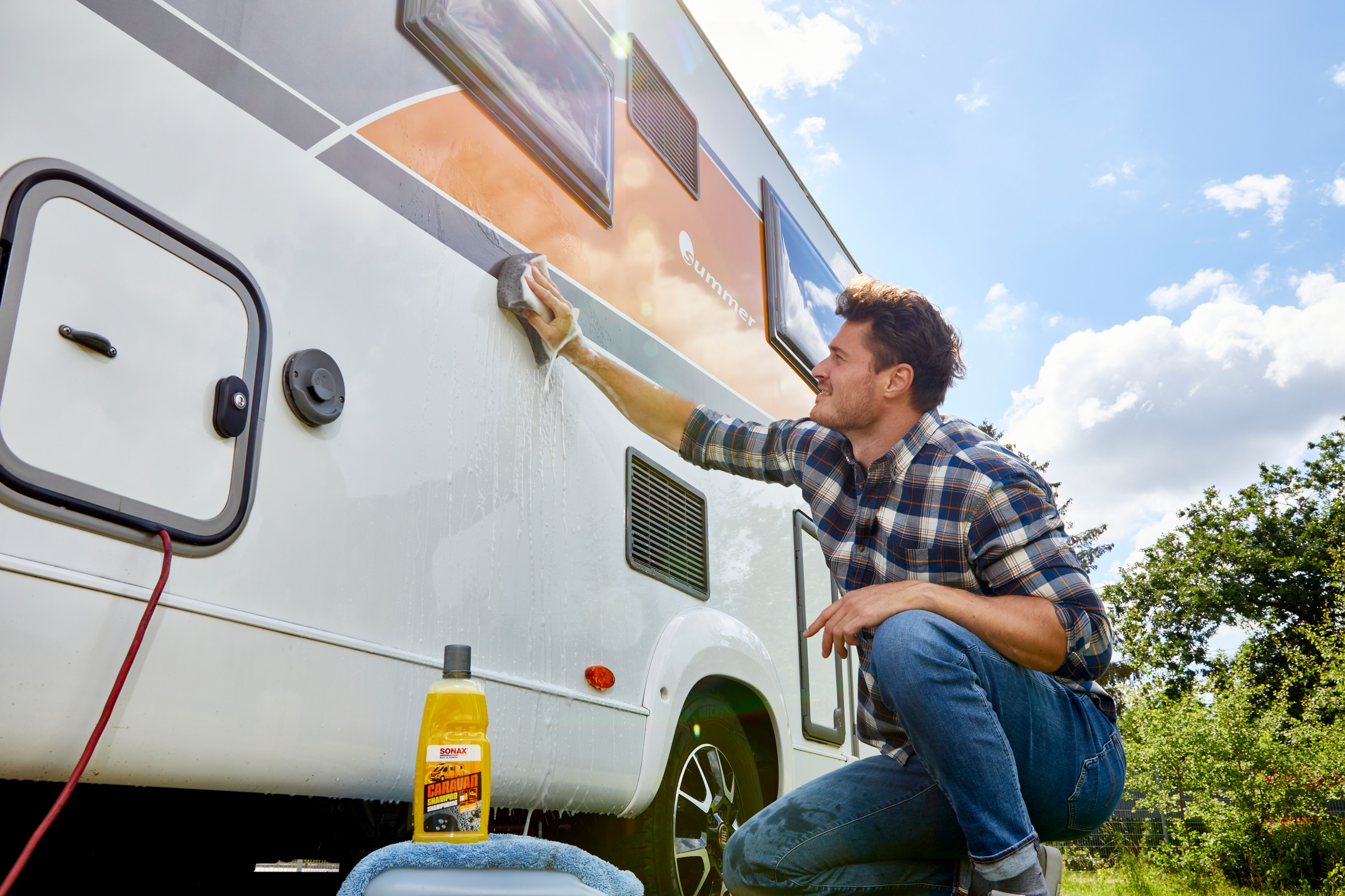 Mann wäscht Wohnmobil mit Schwamm.