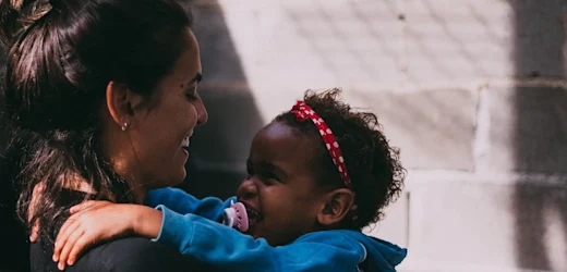 female childcare worker holds up young girl in blue hooded jumper