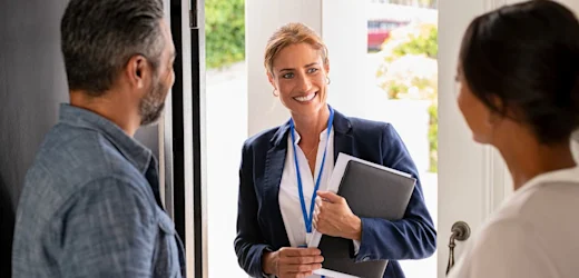 A female case worker visits her clients at their front door with a smile on her face.