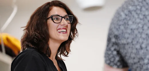 a female personal assistant with medium length brown hair, thick black glasses and red lipstick smiles at work