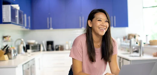A smiling adult works from home in her kitchen as she thinks about how to become a virtual assistant in Australia and her success