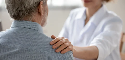 A Community Support Worker smiling and placing her hand on the shoulder of an elderly man with grey hair
