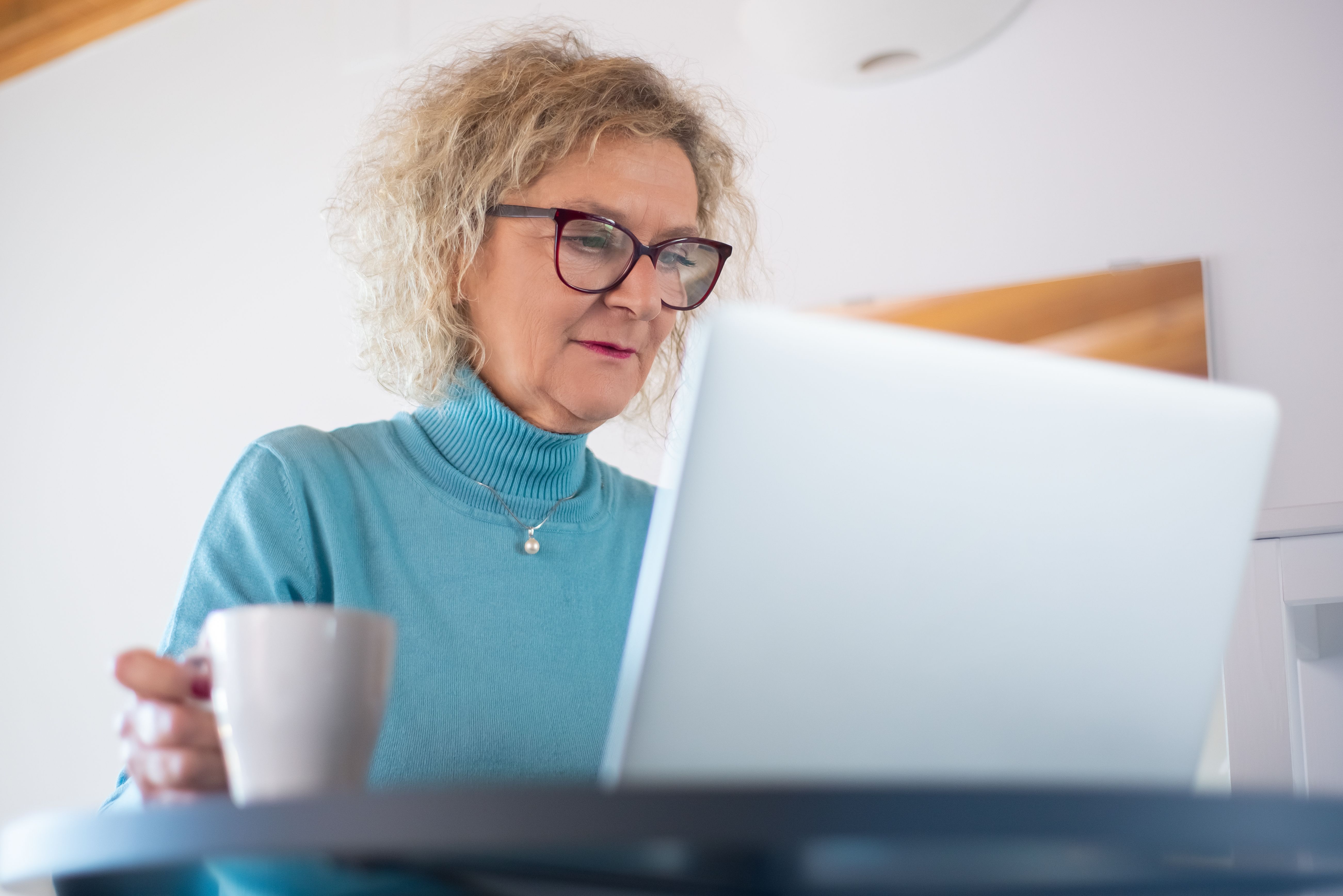 Retired woman working on her laptop with a cup of coffee, focusing on her new career for a retiree.