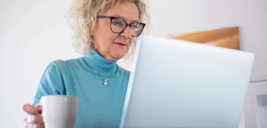 Retired woman working on her laptop with a cup of coffee, focusing on her new career for a retiree.
