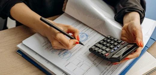 A bookkeeper reviewing financial documents and using a calculator to ensure accurate records for a small business.