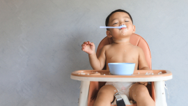 child in a diaper sitting in a high chair with a spoon in their mouth