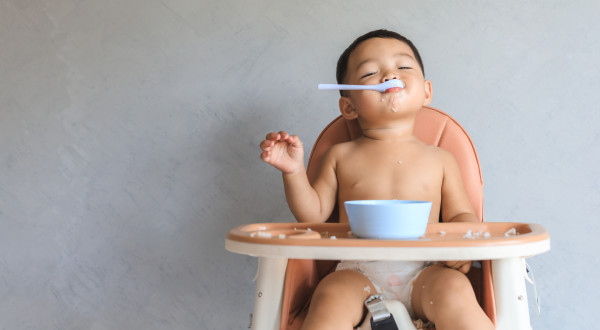 child in a diaper sitting in a high chair with a spoon in their mouth