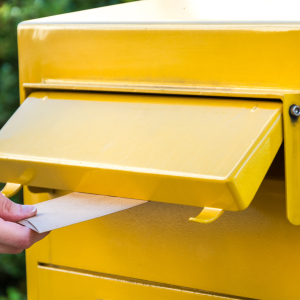 Yellow German mailbox and person putting a letter in