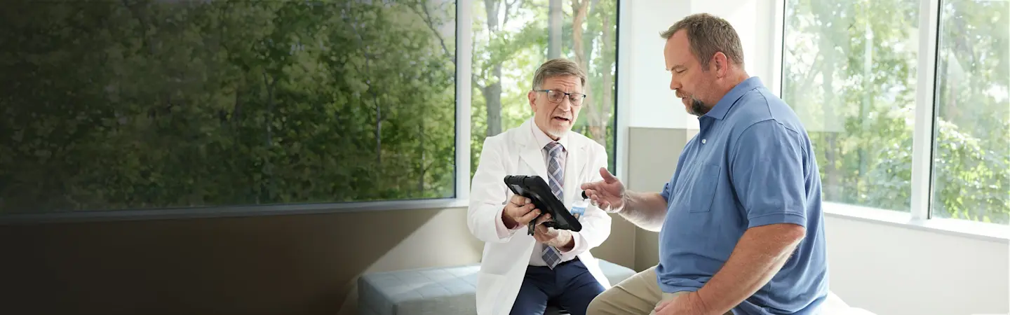 The image features two men in a clinic talking about a procedure displayed on an tablet.