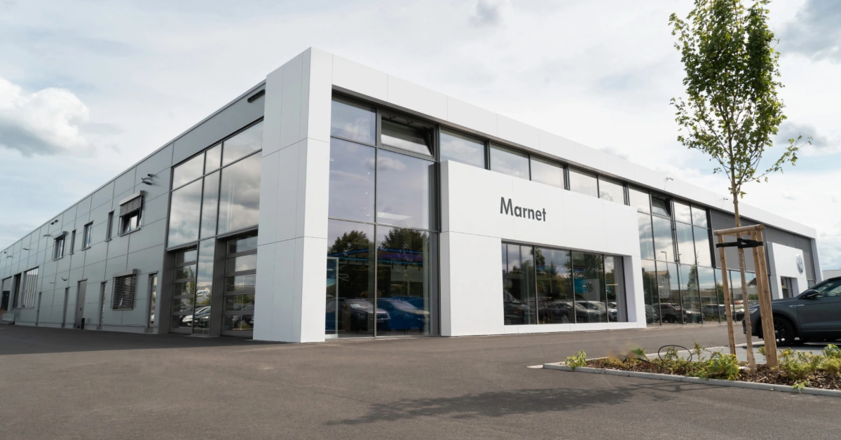 Eine Aufnahme des Volkswagen Autohauses in Wiesbaden, die das Gebäude und Volkswagen Fahrzeuge vor dem Gebäude, sowie die Einfahrt zeigt.