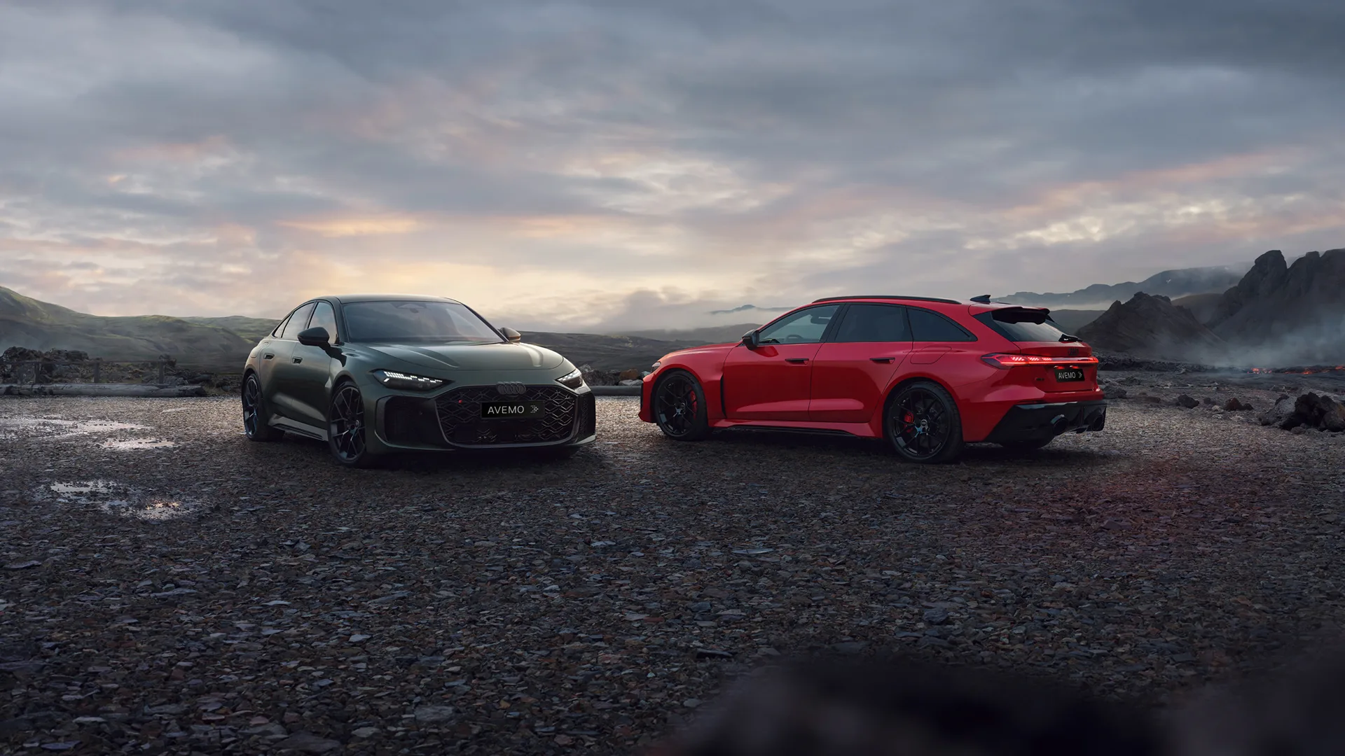 Zwei moderne Sportwagen, ein grüner Audi RS 5 Limousine und ein roter Audi RS 5 Avant, stehen auf einem Schotterweg in einer dramatischen Vulkanlandschaft. Im Hintergrund erheben sich dunkle Berge unter einem dämmrigen Himmel mit weichen Wolken.
