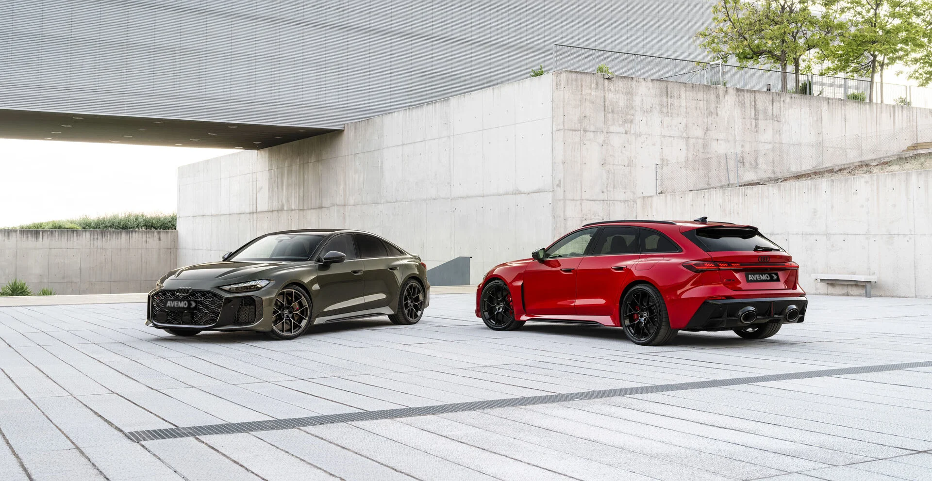 Zwei neue Audi RS 5 Modelle – ein dunkelgrüner Sportback und ein roter Avant – mit AVEMO-Kennzeichen auf einem modernen, minimalistischen Betonplatz. Die Fahrzeuge sind hochwertig ausgeleuchtet und präsentieren ihr sportliches Design.