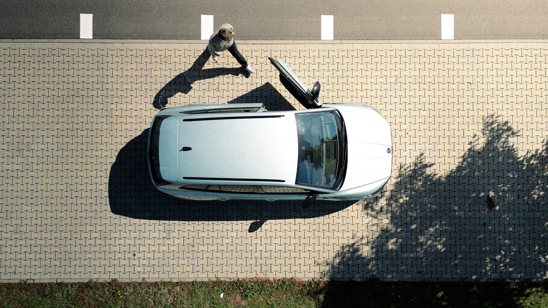 Fahrzeug oben Eine Aufnahme aus Vogelperspektive eines jungen Mannes, der auf ein Auto mit offener Fahrertür zuläuft.