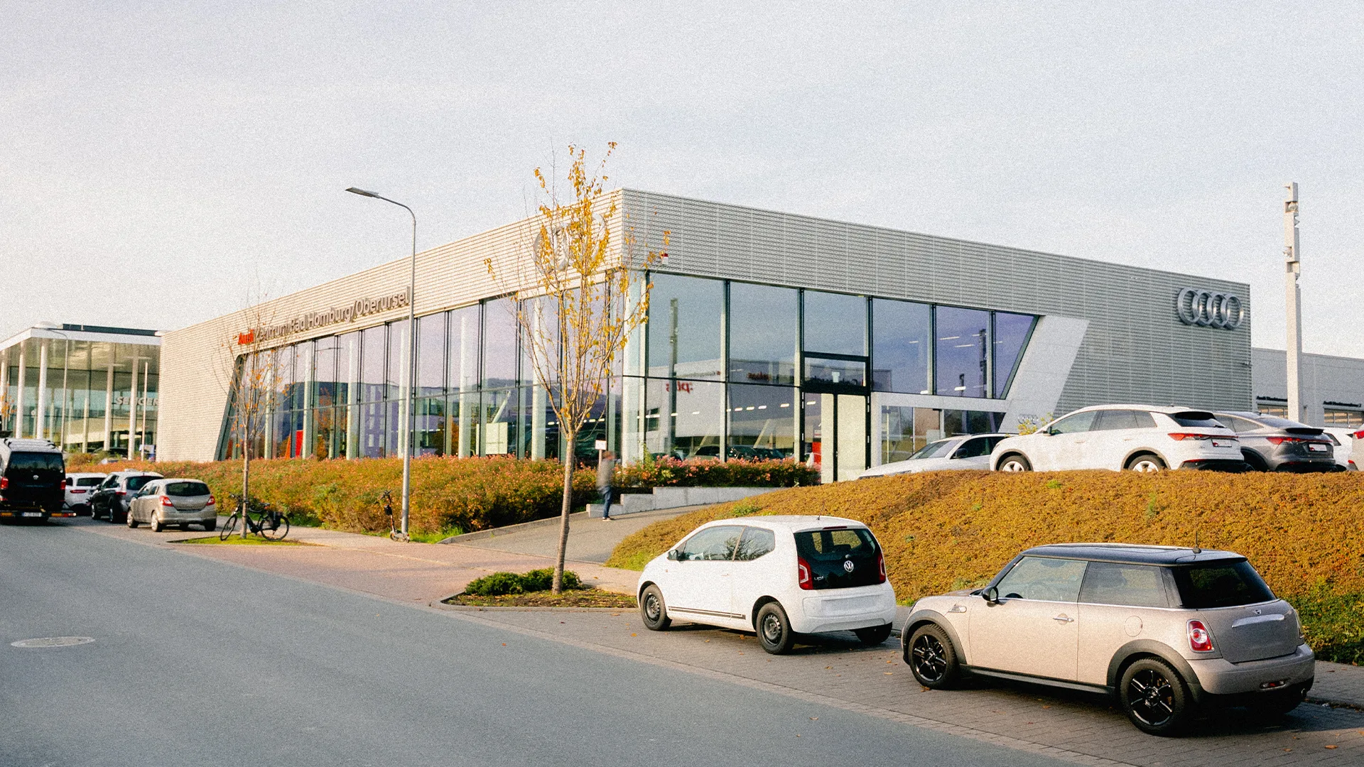Eine Aufnahme des Audi Zentrums in Bad Homburg / Oberursel, dass die Gebäude und Audi Fahrzeuge vor dem Gebäude, sowie die Einfahrt zeigt.