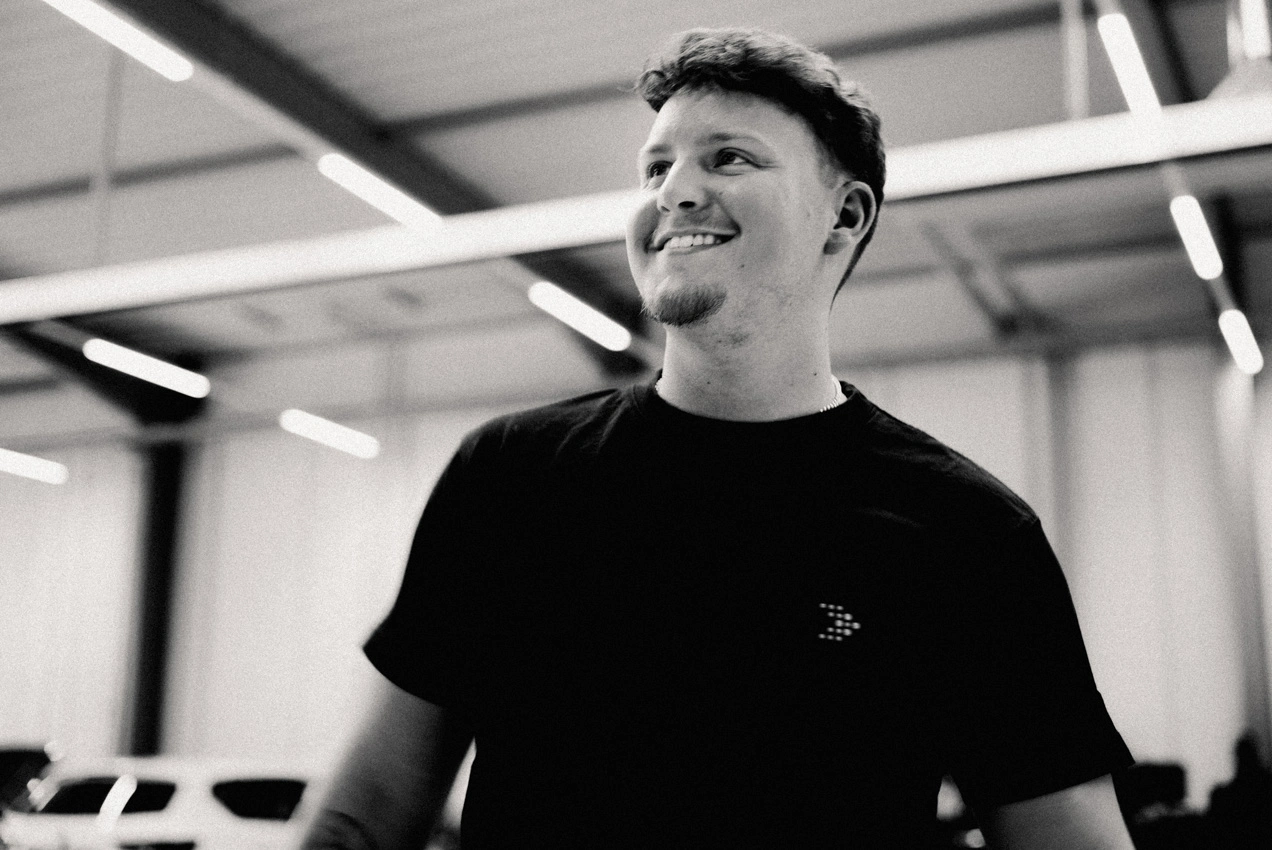 Werkstatt Lachen m-3 Eine Portraitaufnahme eines Mitarbeiters des Autohauses in der Werkstatt. Er lächelt und trägt ein schwarzes AVEMO T-Shirt.