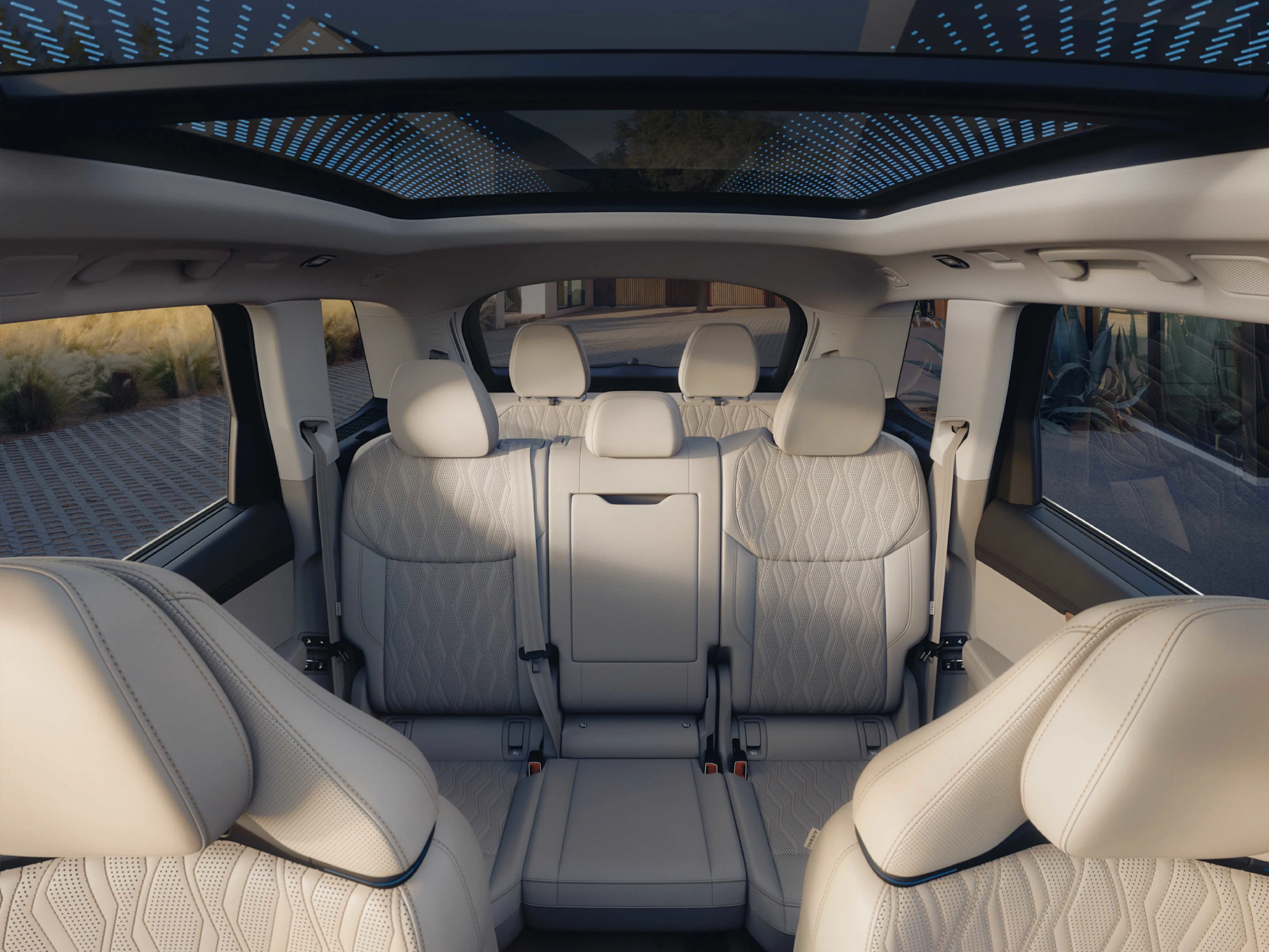 Innenraum-Blick eines Audi Q7 mit hellen Ledersitzen in drei Reihen. Das große Panoramaglasdach über den Sitzen zeigt eine integrierte, blau leuchtende Punkt-Matrix-Struktur.
