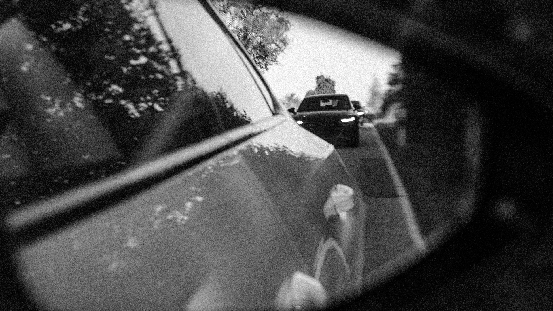 Eine schwarz-weiße Aufnahme des äußeren Rückspiegels eines Fahrzeugs, in dem ein weiteres Fahrzeug zu sehen ist.