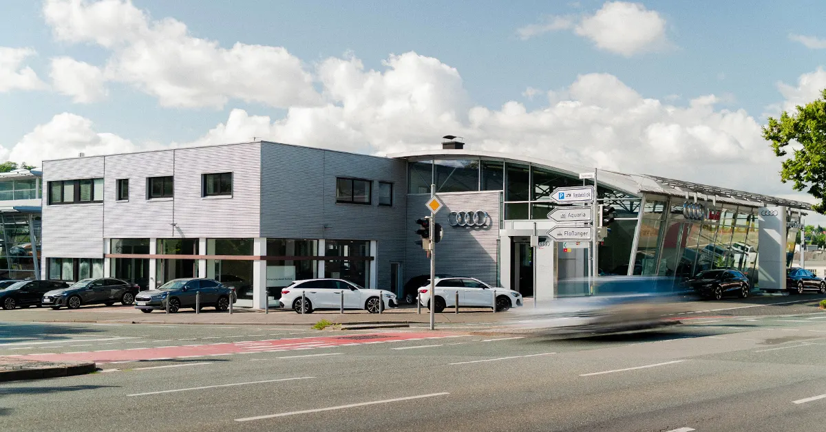 Eine Aufnahme des Audi Autohauses in Coburg, die das Gebäude und Audi Fahrzeuge vor dem Gebäude, sowie die Neustadter Straße zeigt.