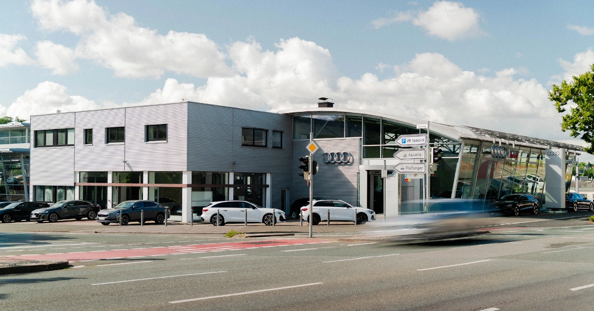 Eine Aufnahme des Audi Autohauses in Coburg, die das Gebäude und Audi Fahrzeuge vor dem Gebäude, sowie die Neustadter Straße zeigt.