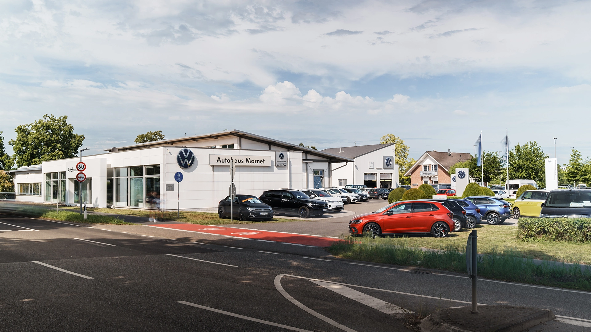 Eine Aufnahme des Volkswagen Autohauses in Bad Nauheim, dass das Gebäude und Volkswagen Fahrzeuge vor dem Gebäude, sowie die Friedberger Straße zeigt.