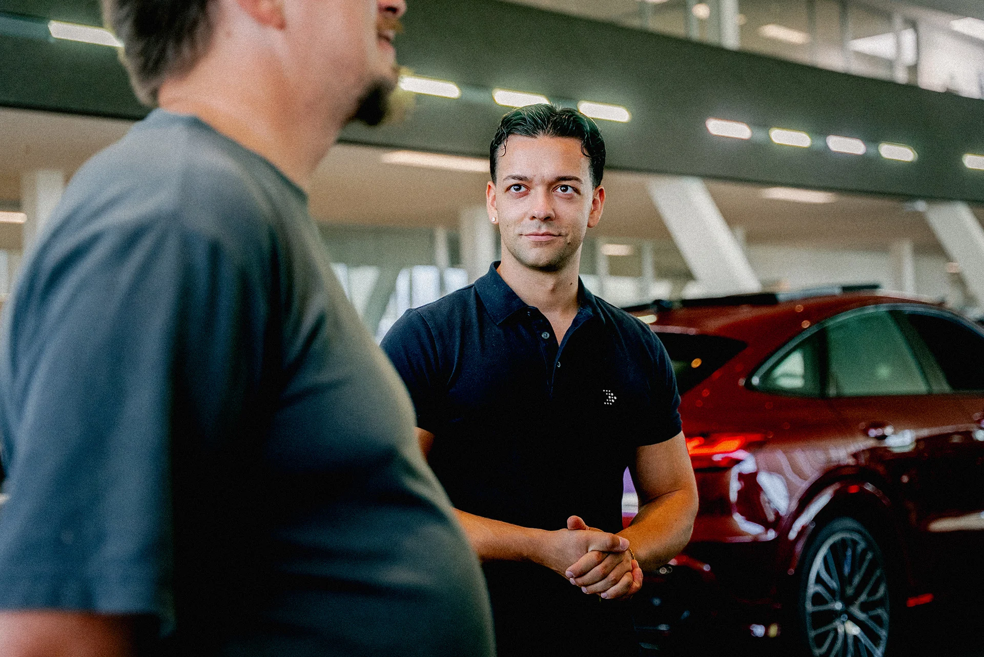 Showroom Konversation m,m Zwei junge Männer unterhalten sich im Audi Showroom. Im Hintergrund ist das Heck eines roten Audi zu sehen und unscharf ein Audi Showroom.