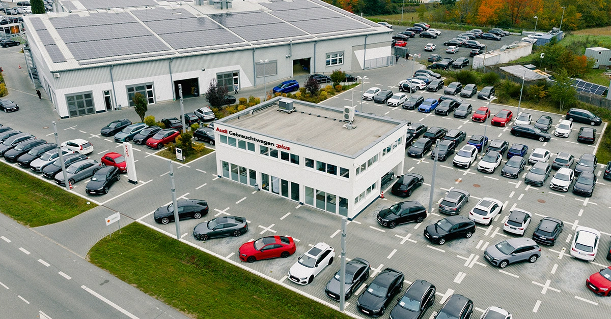 Eine Aufnahme des Audi Autohauses in Mühlheim am Main, die das Gebäude und Audi Fahrzeuge vor dem Gebäude, sowie den Parkplatz zeigt.