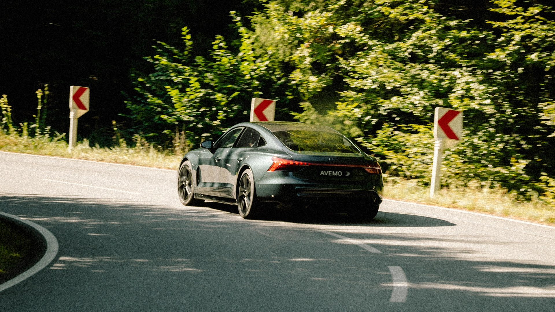 Eine Aufnahme eines Audi Fahrzeugs aus der Heckansicht. Das Fahrzeug fährt auf einer Landstraße in einer S-Kurve.
