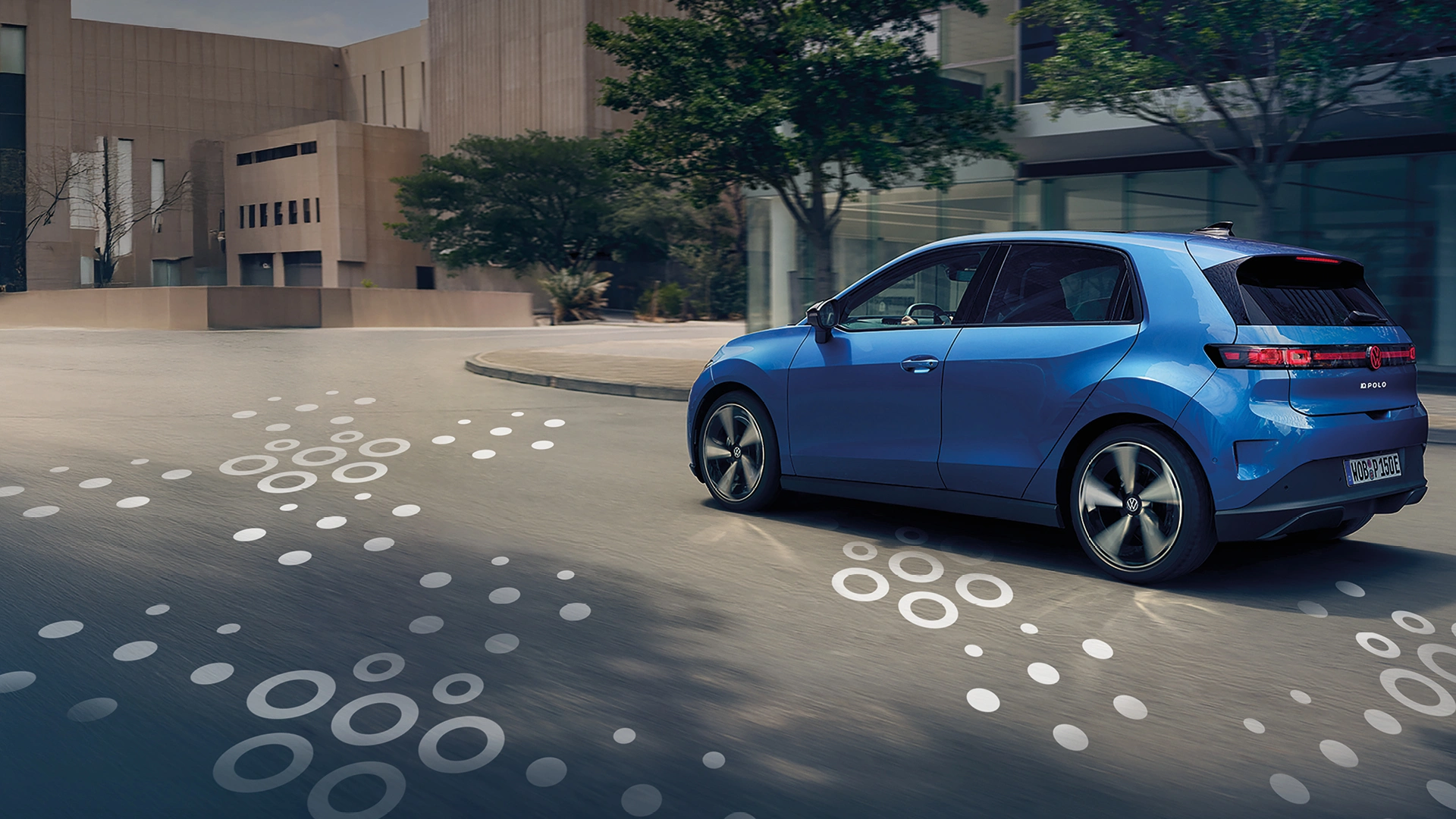 26-077 ID Polo Website Ein blauer Volkswagen ID. Polo fährt durch eine moderne Stadtstraße. Das Heck und die Seite des Fahrzeugs sind zu sehen, während weiße Kreisgrafiken auf dem Asphalt Dynamik andeuten.