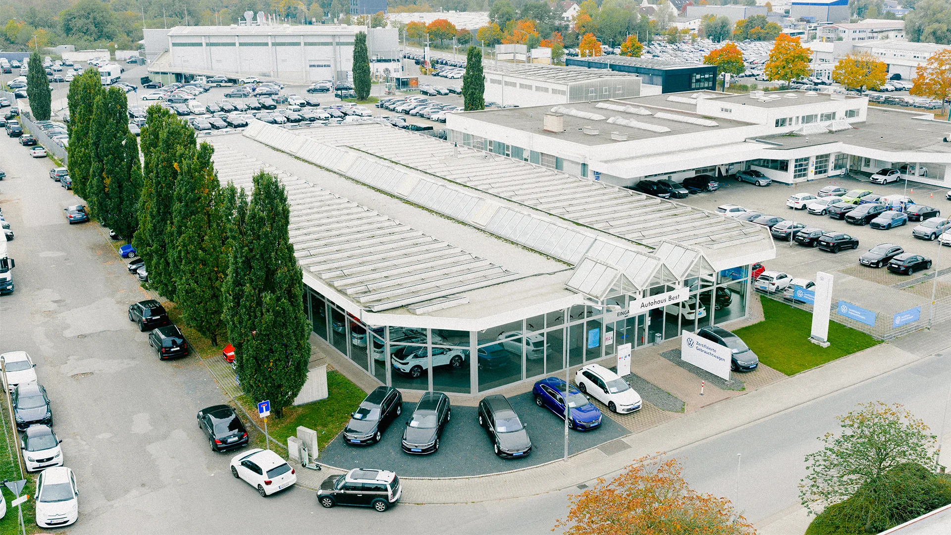 Eine Aufnahme des Volkswagen Gebrauchtwagen Autohauses in Mühlheim am Main, dass die Gebäude und Volkswagen Fahrzeuge vor dem Gebäude, sowie die Einfahrt zeigt.
