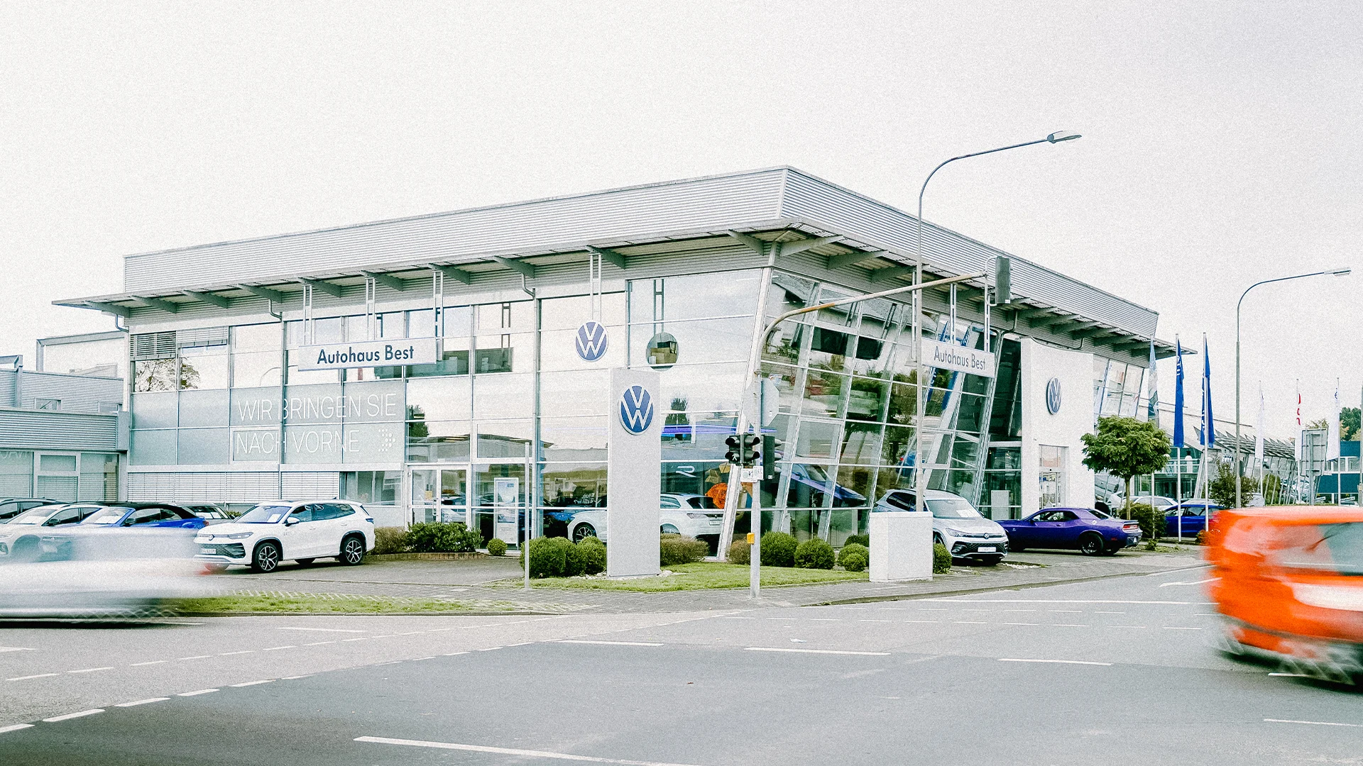 Volkswagen Mühlheim am Main Header Eine Aufnahme des Volkswagen Autohauses in Mühlheim am Main, dass die Gebäude und Volkswagen Fahrzeuge vor dem Gebäude, sowie Parkplätze zeigt.