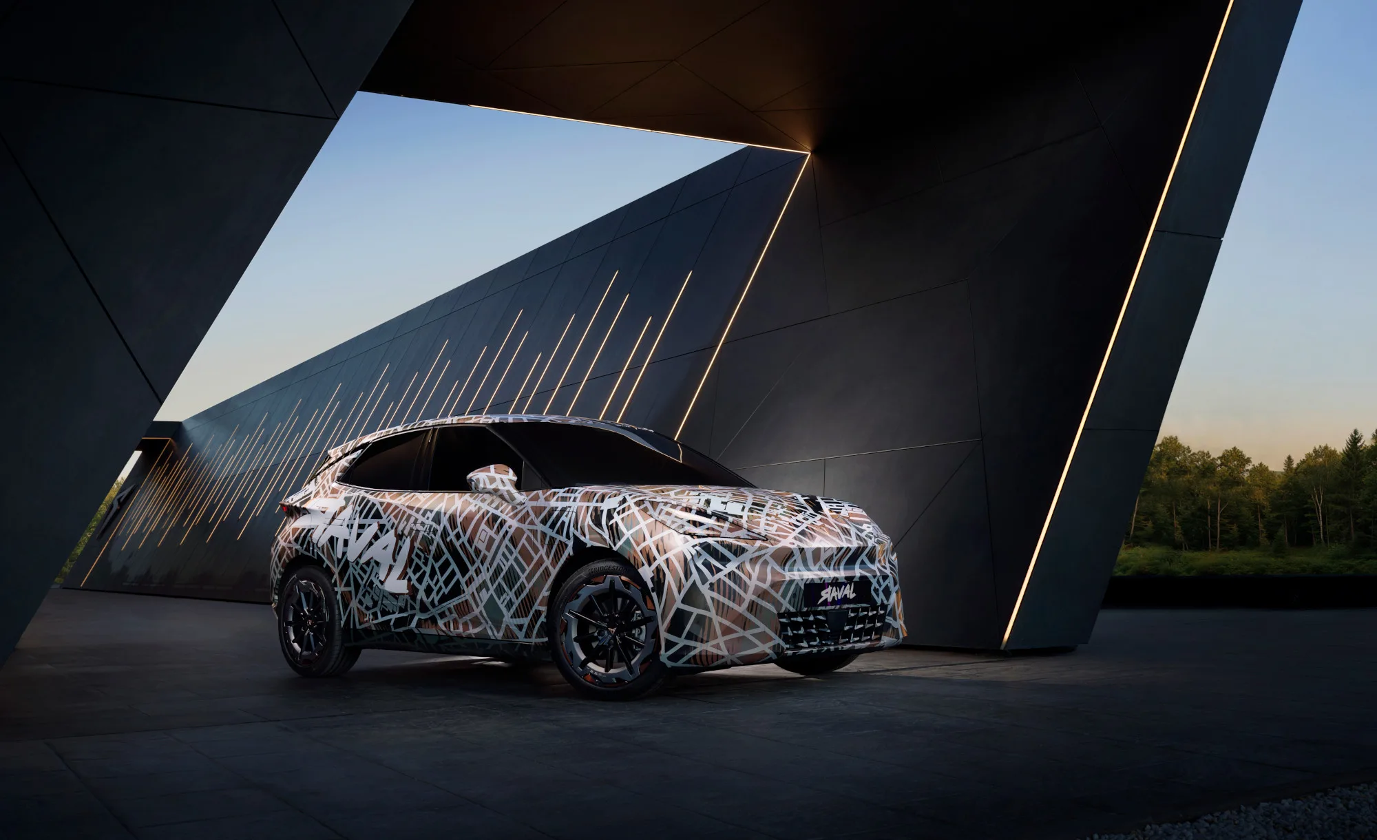 a25-0173-cupra-raval-me-header Dreiviertelansicht eines CUPRA Raval Prototyps auf grauem Hintergrund. Das kompakte Elektroauto ist komplett mit einer schwarz-weißen Tarnfolie im Stadtplan-Design foliert und zeigt markante kupferfarbene Akzente an den Felgen und Logos.