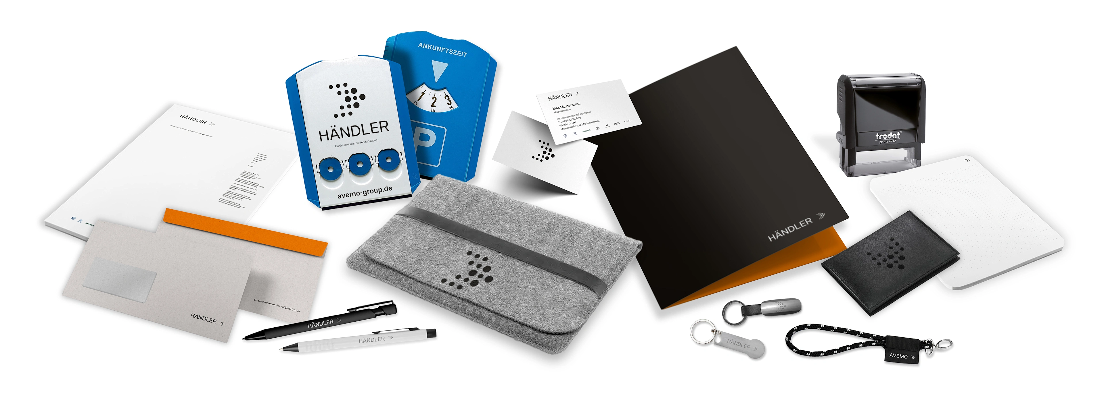 Übersicht verschiedener Corporate Identity (CI) Artikel für Händler mit dem AVEMO Group Logo: Briefpapier, Umschläge, Visitenkarten, Notizblöcke, Stifte, ein graues Filz-Etui, Notizbuch, ein schwarzes Lederetui, Schlüsselanhänger und ein Stempel.