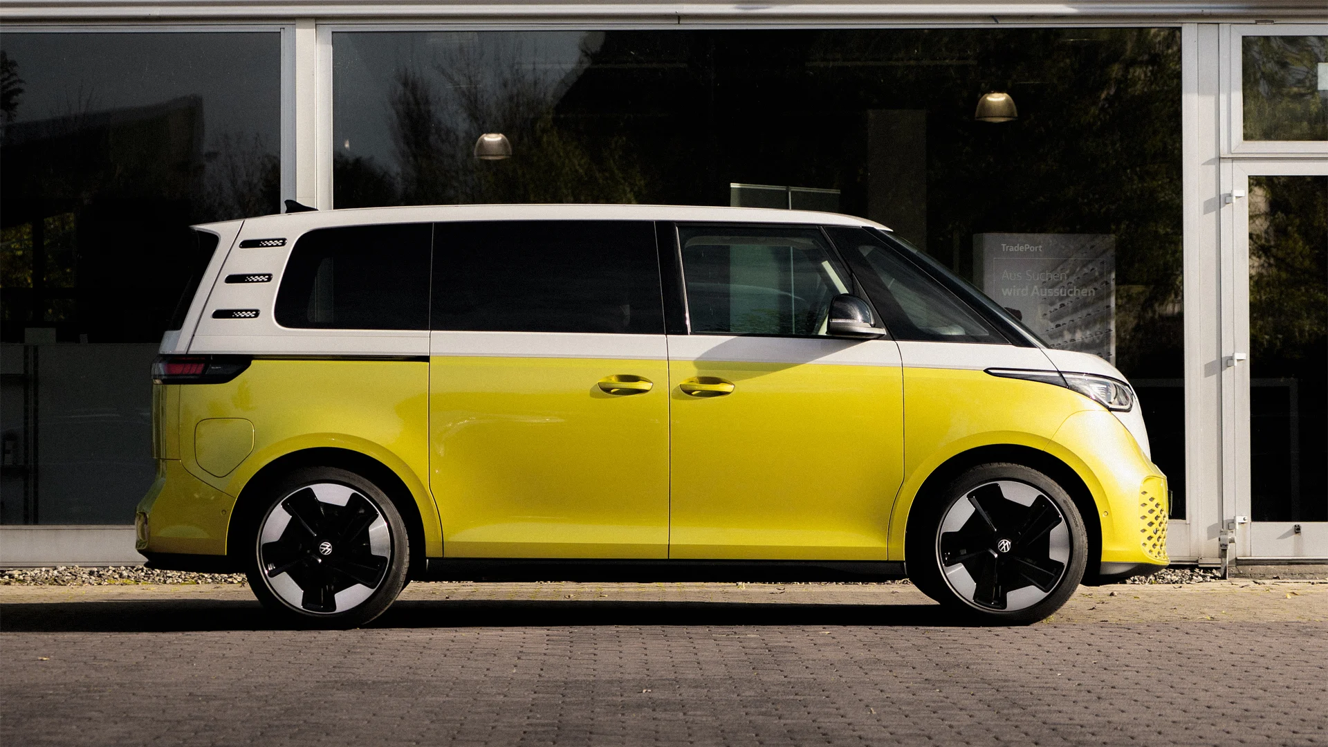 Eine Aufnahme eines gelb-weißen Volkswagen ID. Buzz, der vor einem Autohaus mit einer Glasfront seitlich steht.