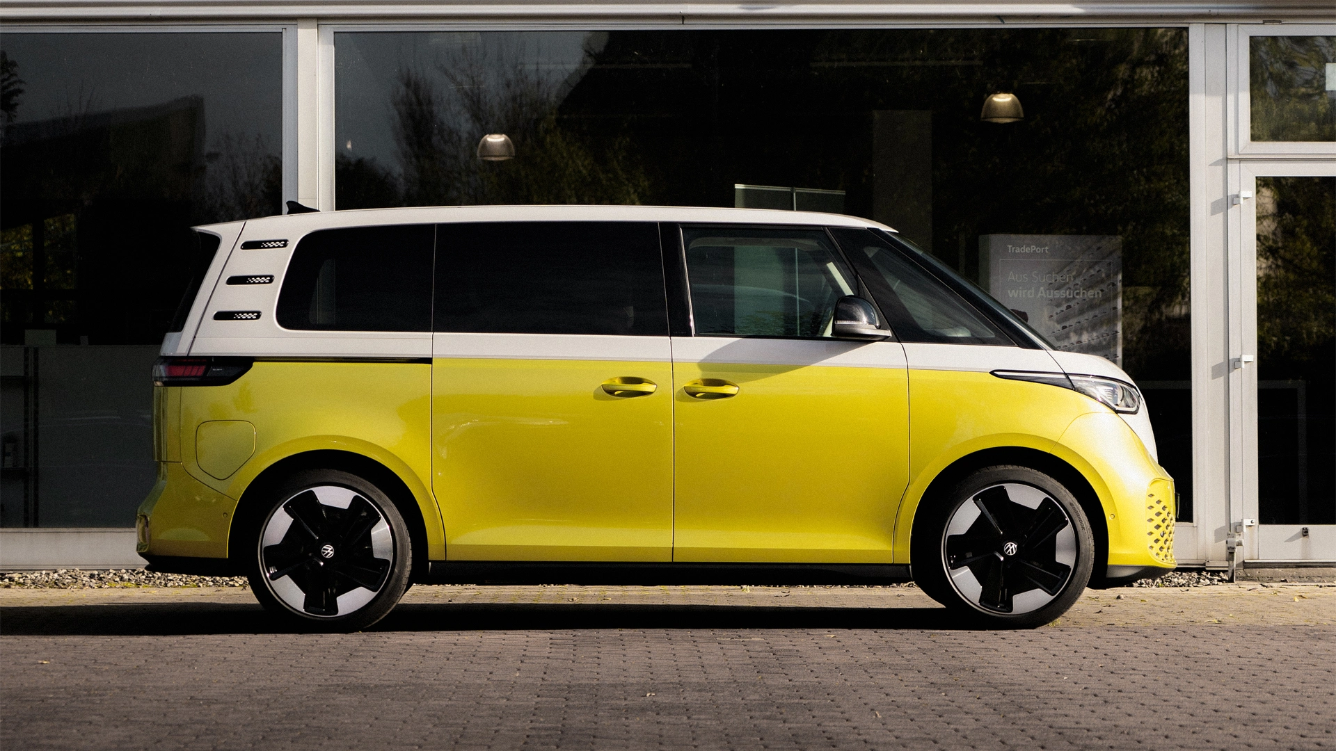 Eine Aufnahme eines gelb-weißen Volkswagen ID. Buzz, der vor einem Autohaus mit einer Glasfront seitlich steht.