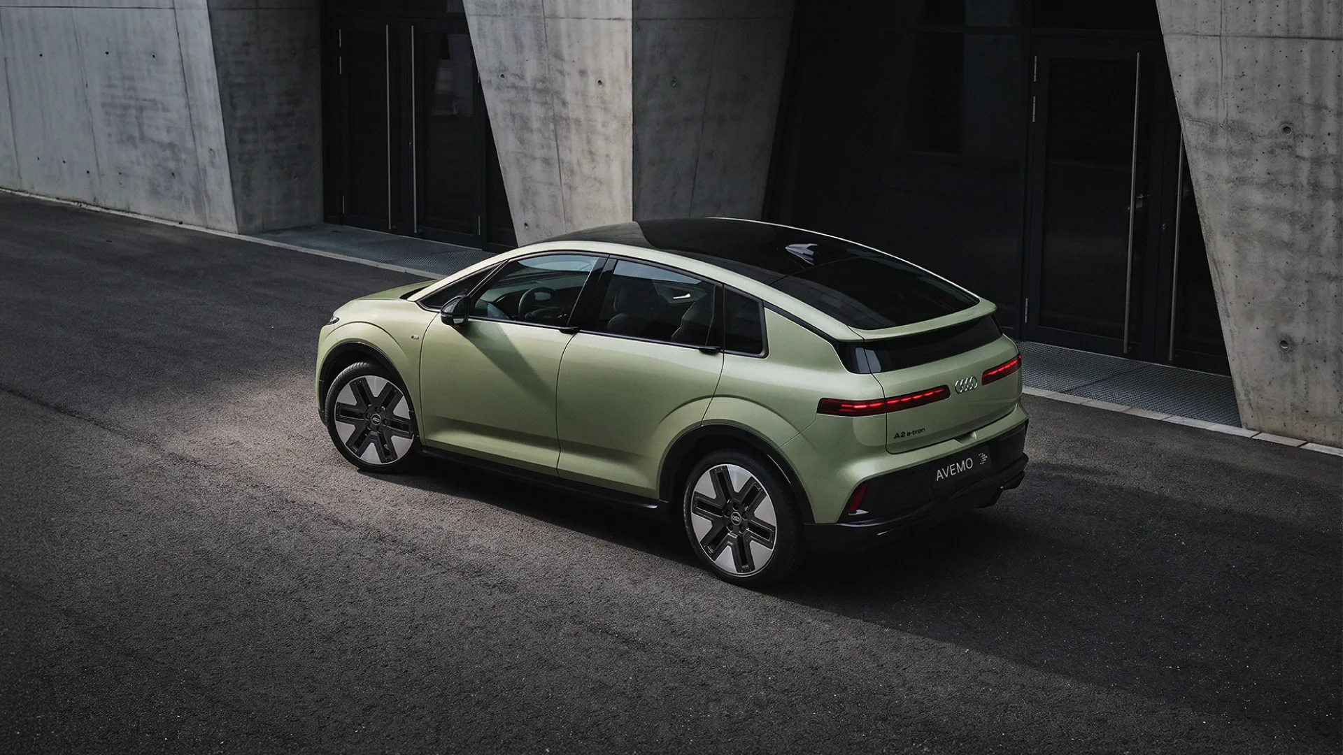 Ein hellgrüner Audi SUV-Coupé parkt von oben gesehen vor einer modernen Betongefäude-Fassade. Das Fahrzeug hat ein dunkles Panorama-Glasdach und das Kennzeichen AVEMO.