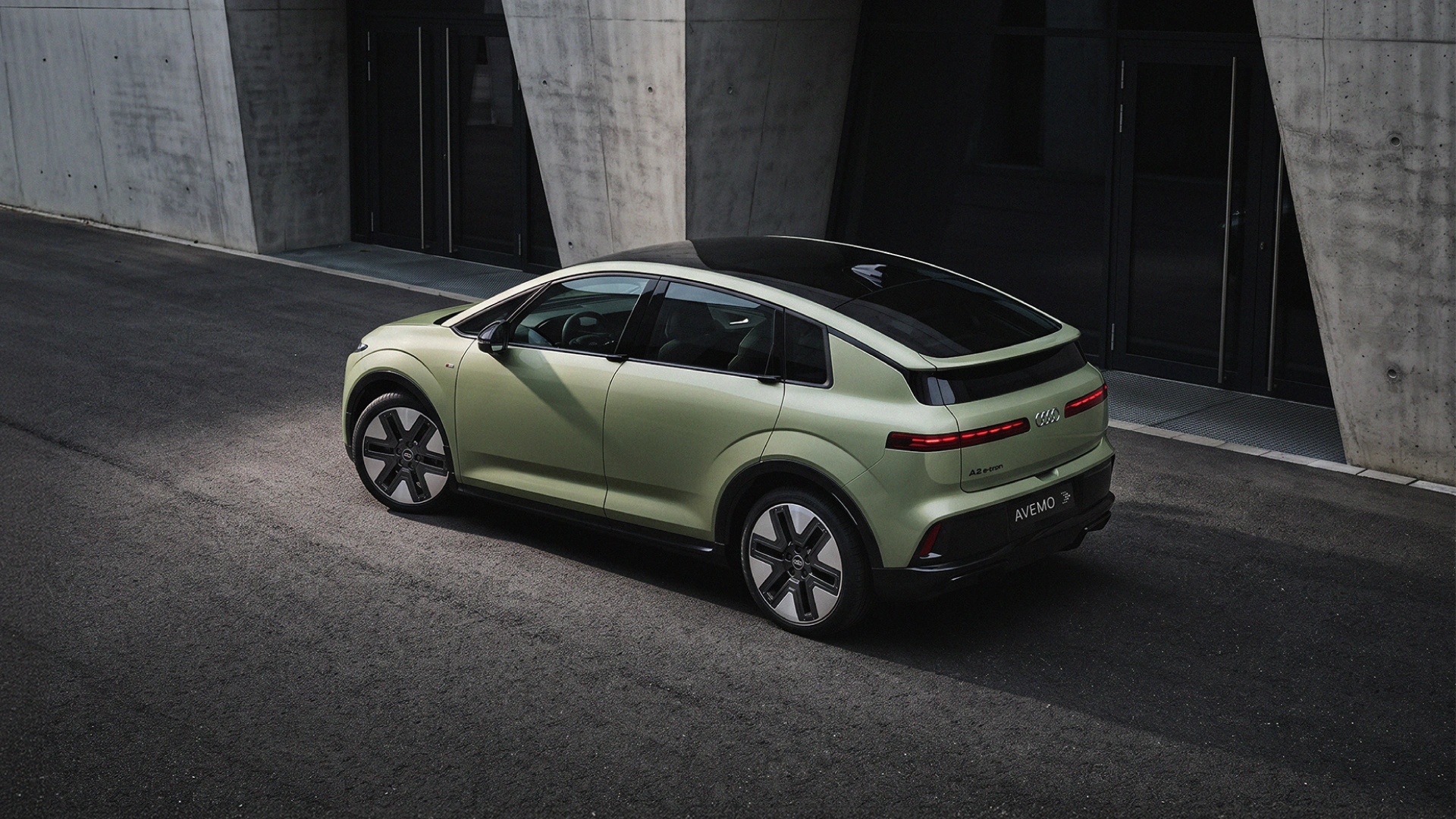 Ein hellgrüner Audi SUV-Coupé parkt von oben gesehen vor einer modernen Betongefäude-Fassade. Das Fahrzeug hat ein dunkles Panorama-Glasdach und das Kennzeichen AVEMO.