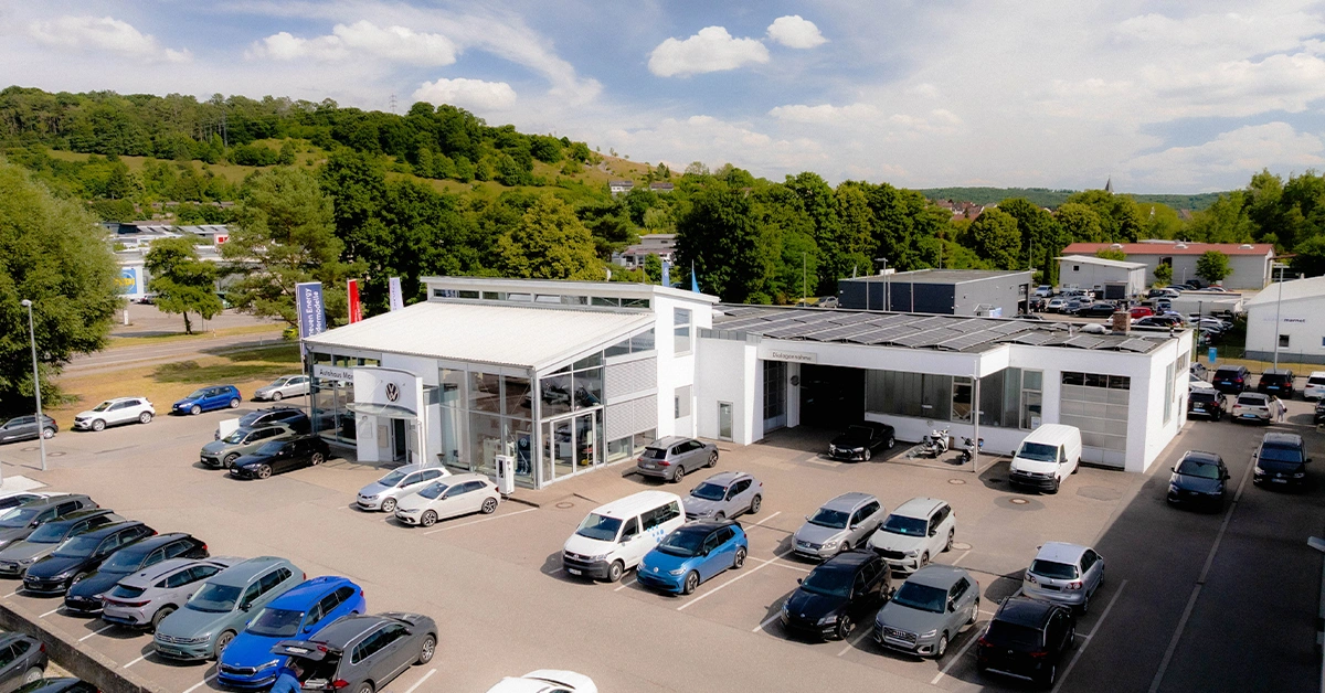 Eine Aufnahme des Volkswagen Autohauses in Heidenheim, die das Gebäude und Volkswagen Fahrzeuge vor dem Gebäude, sowie den Parkplatz zeigt.