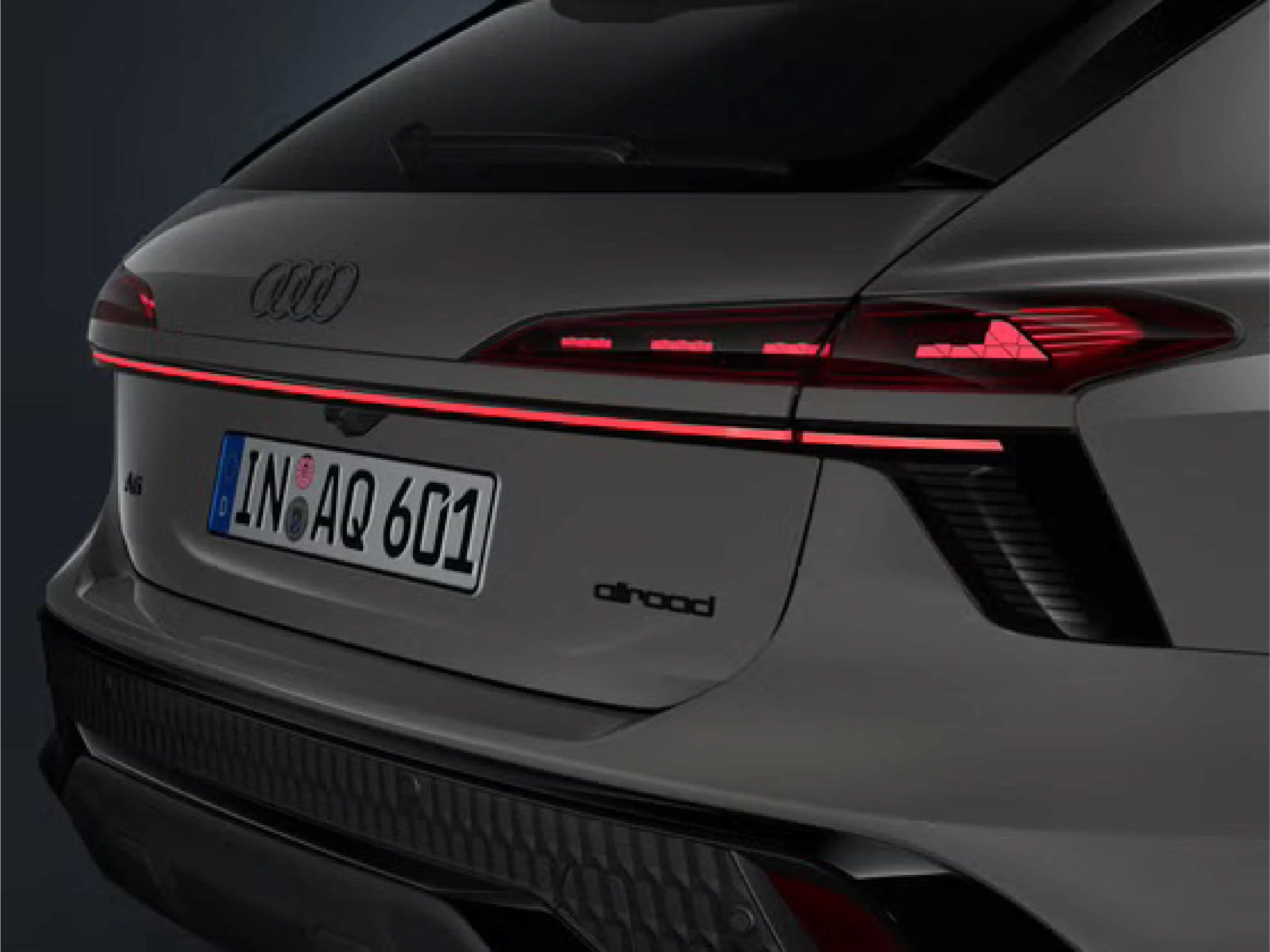 Nahaufnahme des Hecks eines grauen Audi allroad mit dem Kennzeichen „IN AQ 601“. Zu sehen sind die vier Audi-Ringe, der „allroad“-Schriftzug und das durchgehende, schmale rote LED-Leuchtenband im eingeschalteten Zustand.