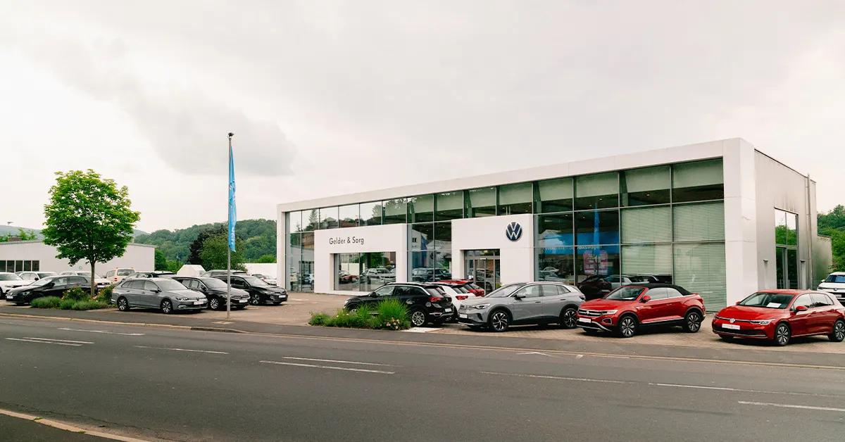 Eine Aufnahme des Volkswagen Autohauses in Bad Kissingen, die das Gebäude und Volkswagen Fahrzeuge vor dem Gebäude, sowie die Würzburger Straße zeigt.