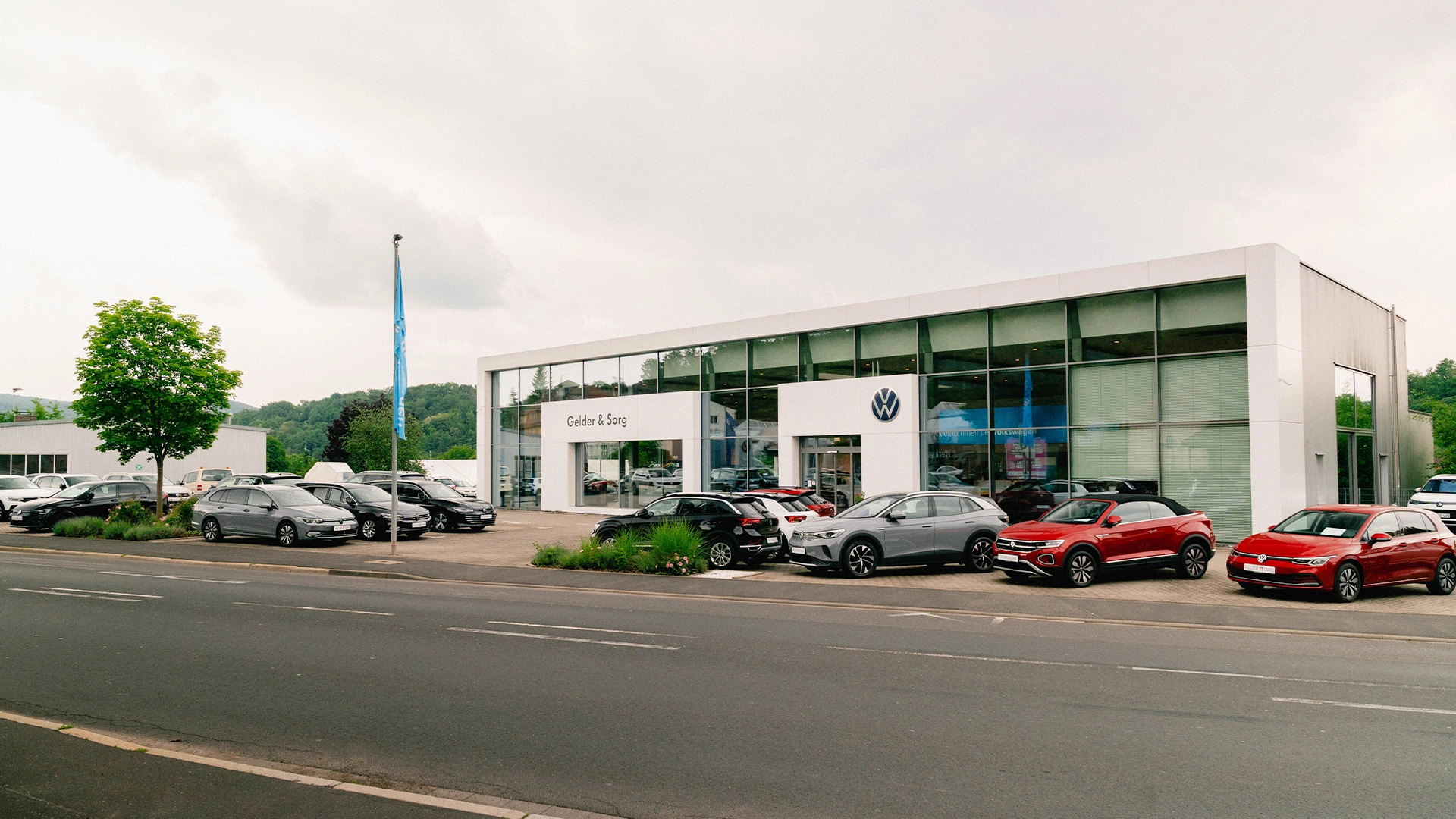 Eine Aufnahme des Volkswagen Autohauses in Bad Kissingen, die das VW-Gebäude, den Haupteingang  sowie die Volkswagen Fahrzeuge vor dem Autohaus zeigt.
