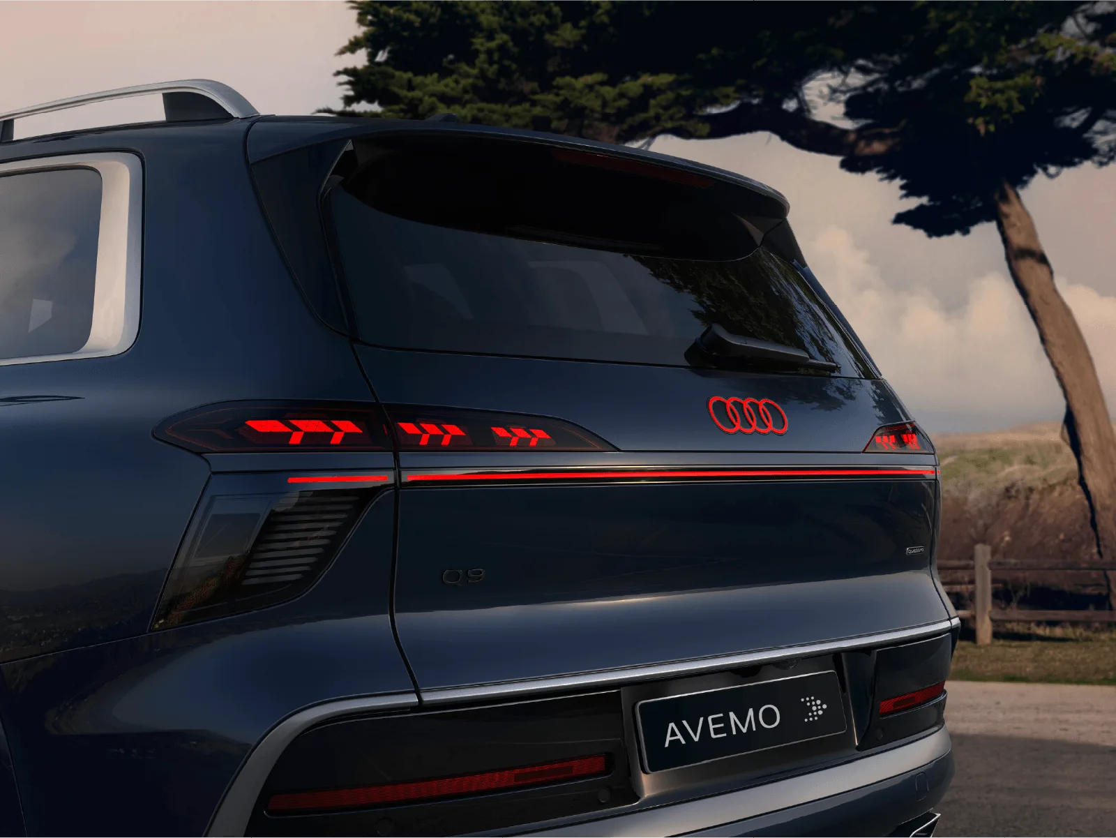 Heckansicht eines dunkelblauen Audi Q9 mit rot leuchtenden Audi-Ringen, durchgehendem LED-Lichtband und modernen Rückleuchten. Auf dem Nummernschild steht „AVEMO“.