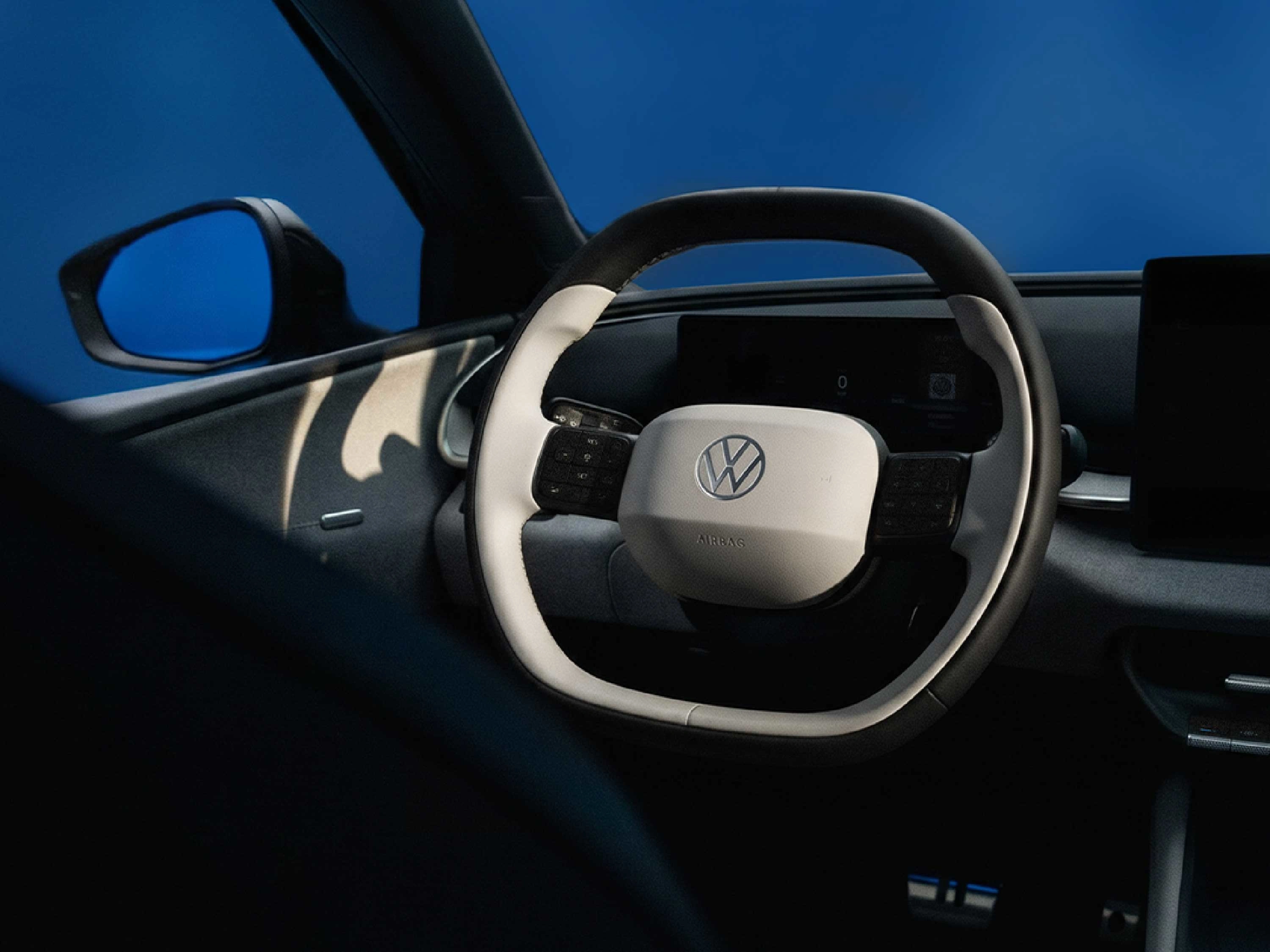 Blick in das moderne Cockpit eines VW ID.Polo. Im Fokus steht das zweifarbige Multifunktionslenkrad in Weiß und Schwarz mit VW-Logo, flankiert von digitalen Displays. Durch das Seitenfenster ist ein blauer Hintergrund sichtbar.