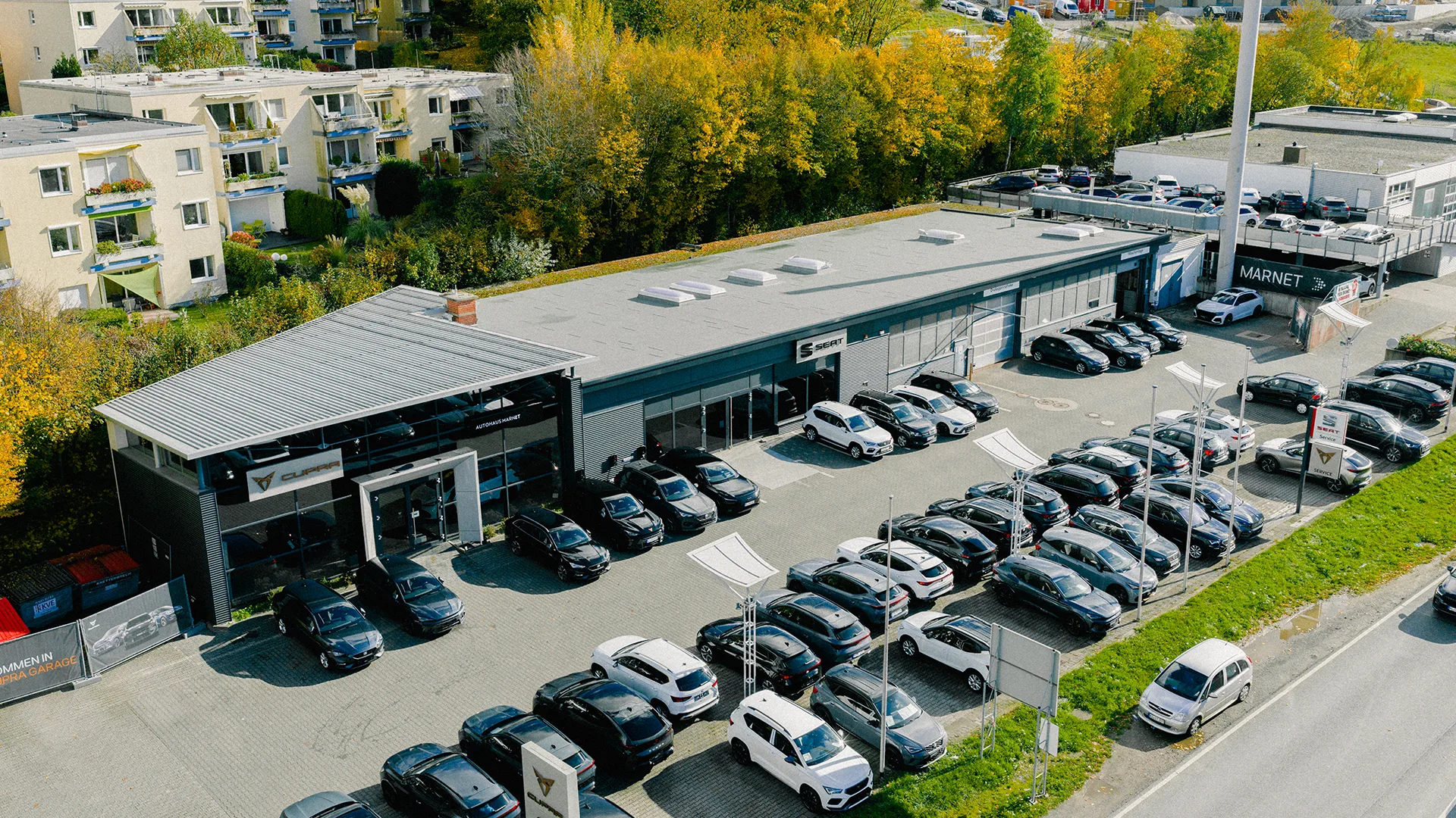 Eine Aufnahme des SEAT & CUPRA Autohauses in Königstein im Taunus, dass die Gebäude und SEAT und CUPRA Fahrzeuge vor dem Gebäude, sowie die Einfahrt zeigt.