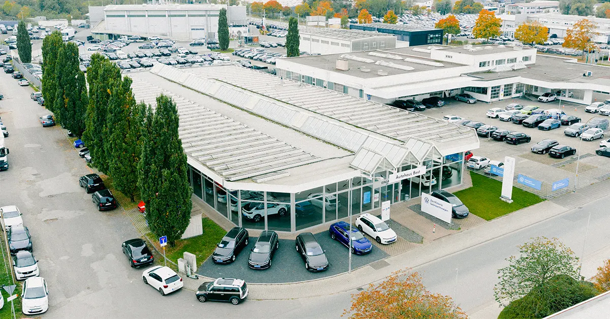 Eine Aufnahme des Volkswagen Gebrauchtwagen Autohauses in Mühlheim am Main, die das Gebäude und Volkswagen Fahrzeuge vor dem Gebäude, sowie die Einfahrt zeigt.