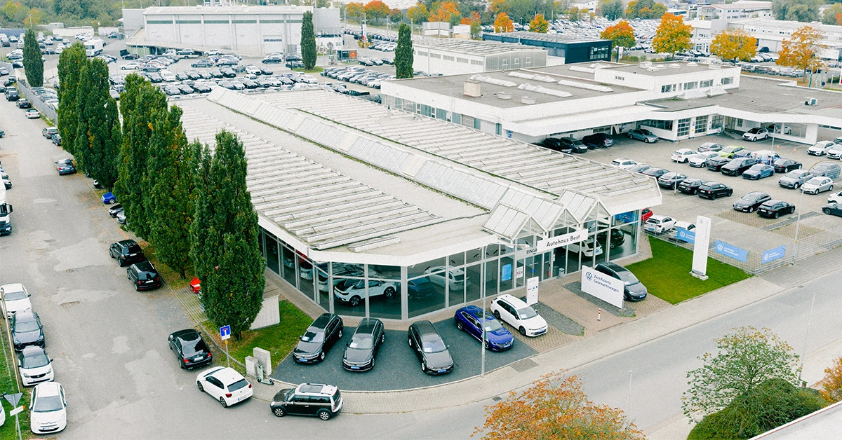 Eine Aufnahme des Volkswagen Gebrauchtwagen Autohauses in Mühlheim am Main, die das Gebäude und Volkswagen Fahrzeuge vor dem Gebäude, sowie die Einfahrt zeigt.